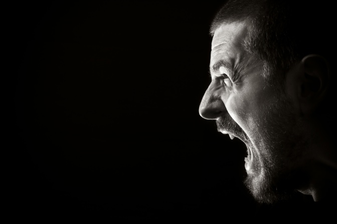 Portrait of screaming angry man on black background